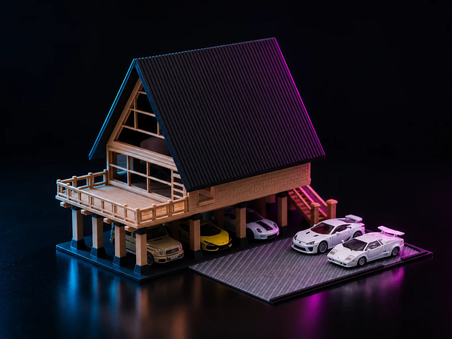 A printed A-frame house lit in cyan and magenta, raised on timber piers with a steep dark gable, a railed deck and cars parked underneath.