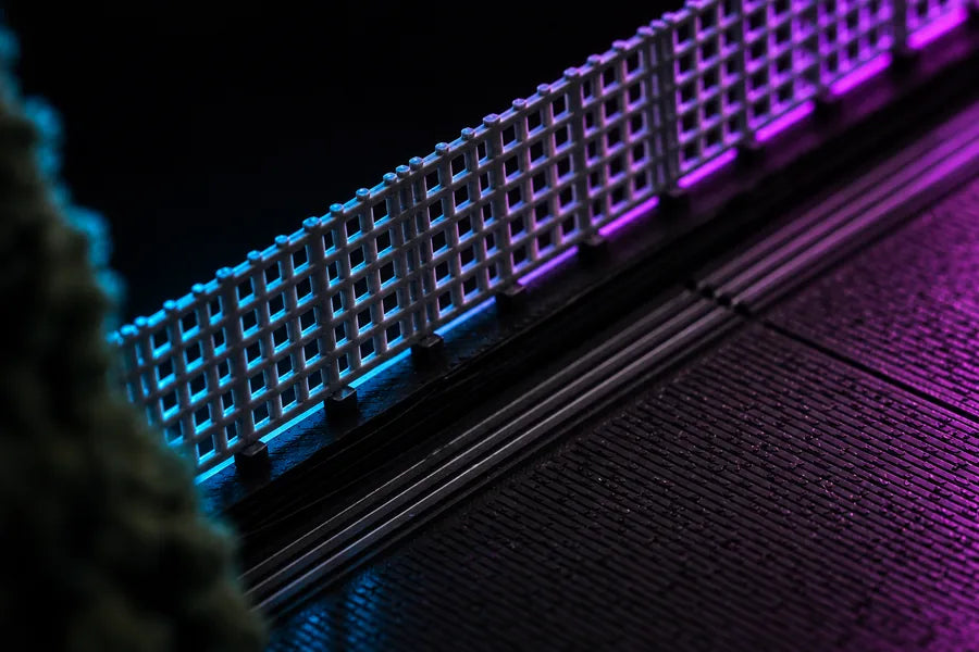 Frame 3 — close on the fence, the open square weave lit blue at one end and magenta at the other, a scored panel line running away behind it.