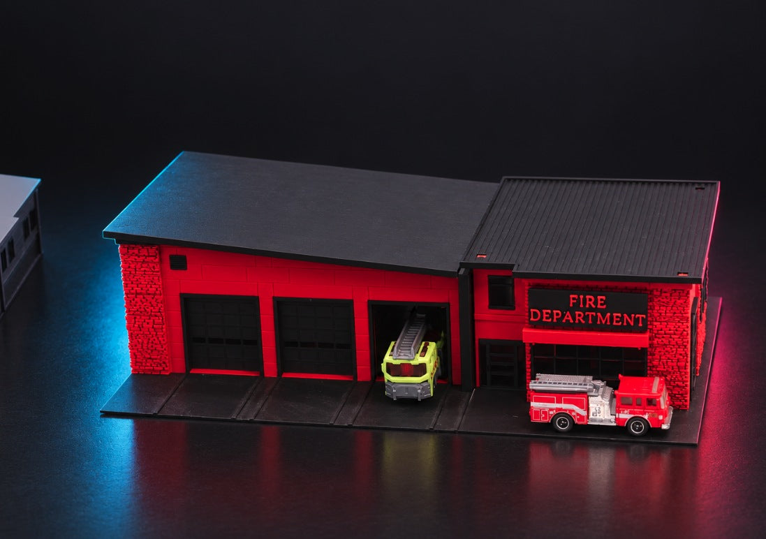 Red and black fire station diorama with three truck bays, a FIRE DEPARTMENT sign and fire trucks, studio shot