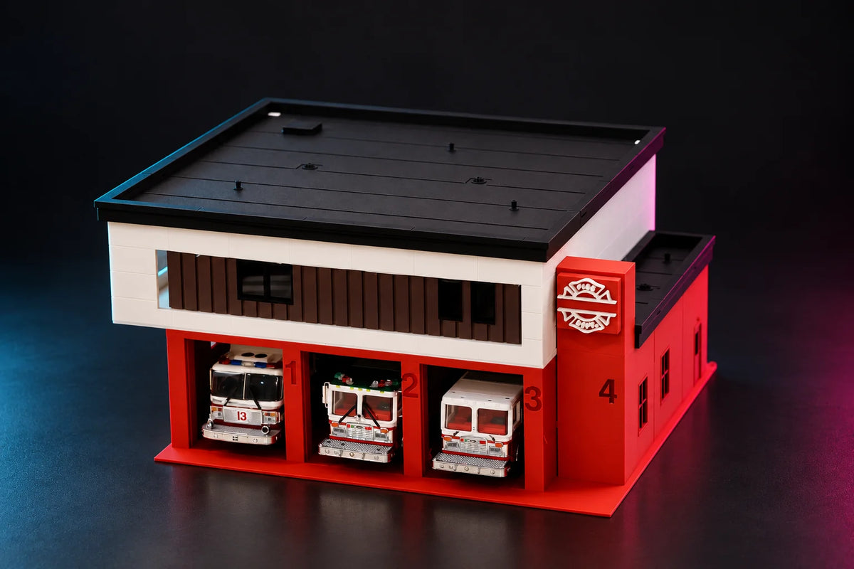 Modern two-story 1:64 fire station diorama in red and white, three diecast fire engines parked in the numbered bays