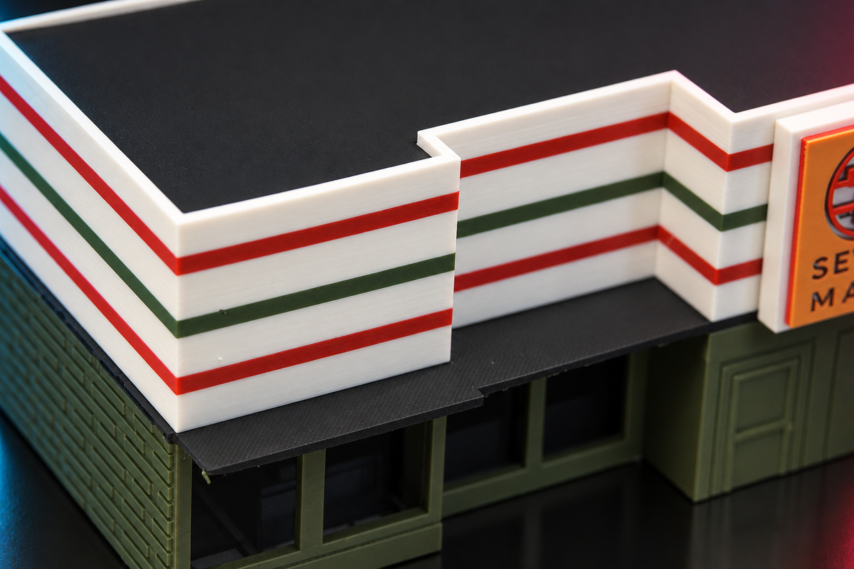 Close-up of the white, red and green striped walls and black roof of the 1:64 Seven Mart