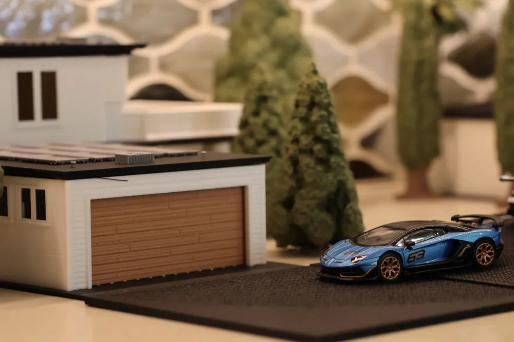 A white two-storey printed house with its timber garage door closed and a blue supercar parked alongside, conifers behind.