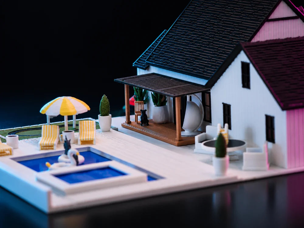 Looking down on the deck: a rectangular blue pool set into white paving, a yellow and white parasol, white chairs and planters, and the porch roof cutting across the top of the frame.