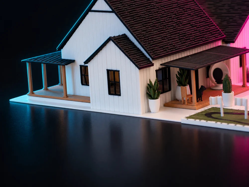 The same house seen straight across the front at deck height, warm light raking along the white boards and the porch posts, a white rail and a small conifer at the right.