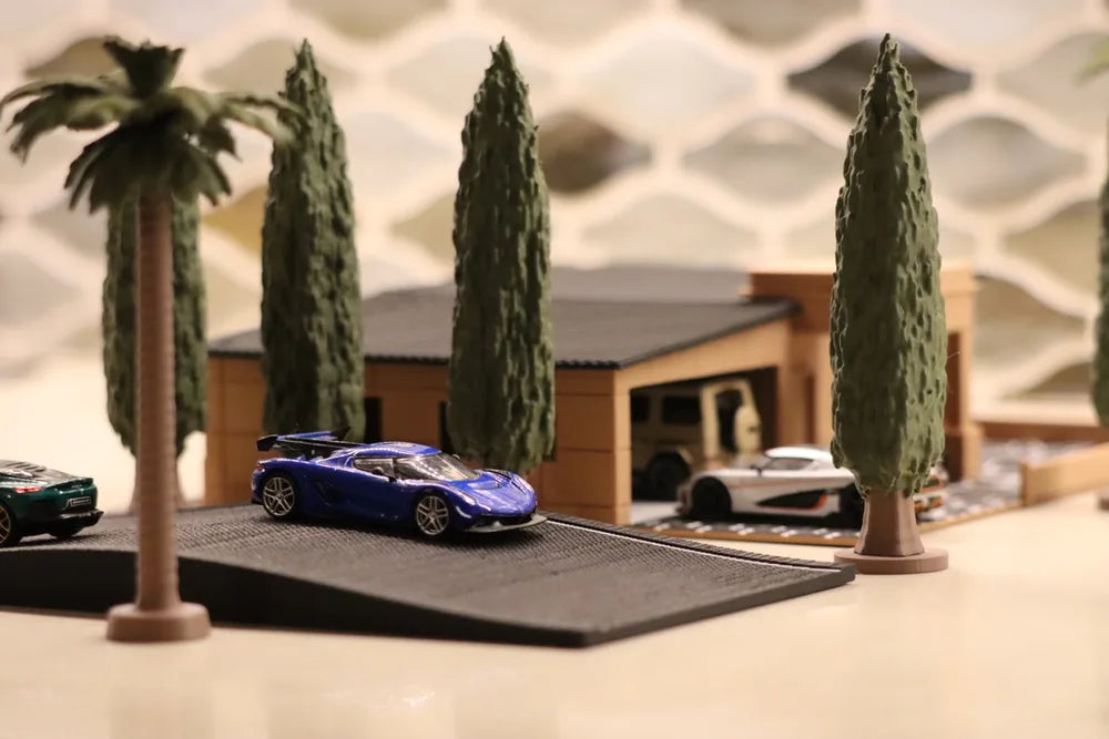 A printed street scene: palms and tall cypress along a grey paved drive, a blue-violet sports car in the middle of the frame, a low timber-clad house to the right with an open garage bay, and two more cars at the edges.
